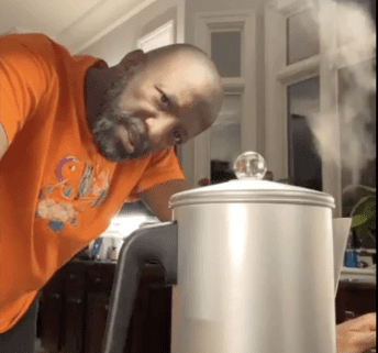 Man in kitchen with steaming coffee pot.