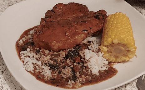 Steak with rice, sauce, and corn cob.
