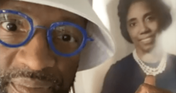 Man with blue glasses, holding a portrait.