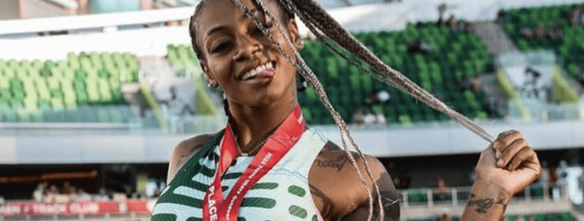 Screenshot-2023-07-17-at-10.09.15-AM-845x321 Athlete smiling with medal in stadium.