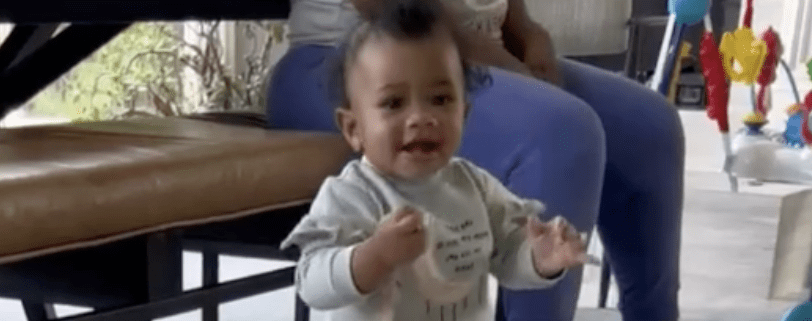 Baby standing and smiling indoors.