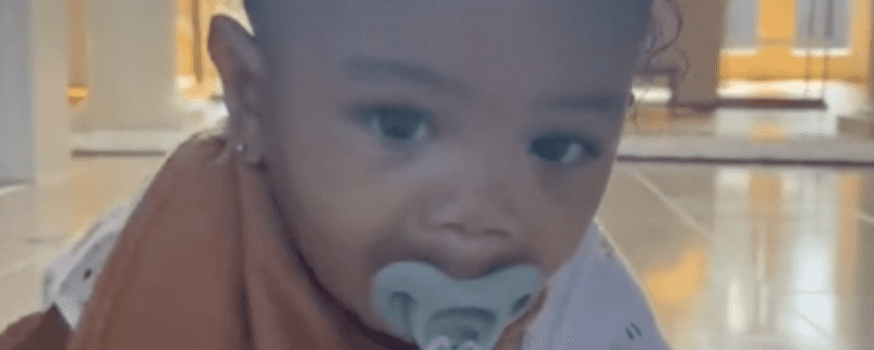 Baby with pacifier crawling indoors.