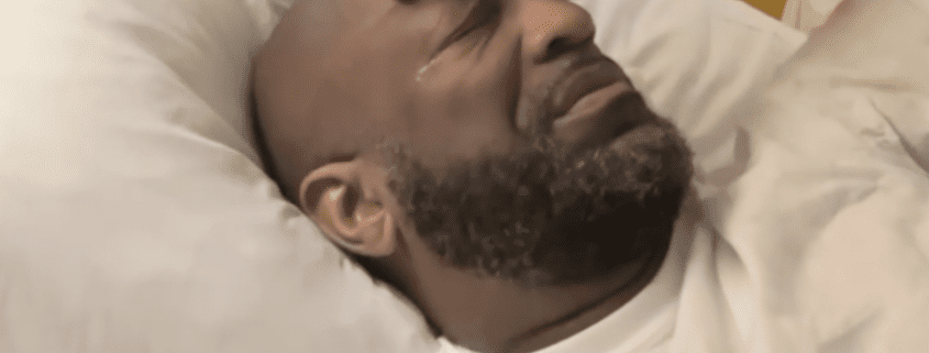 Man lying in bed, appearing emotional.