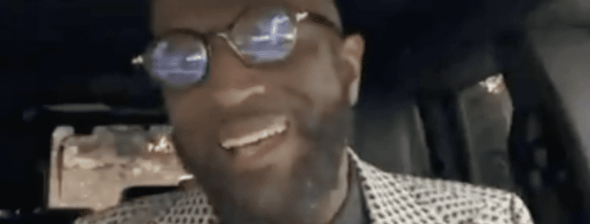 Man smiling inside a vehicle, wearing glasses.